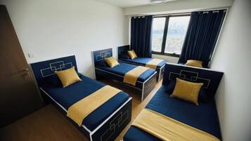 Habitación de hotel con tres camas alineadas, un ventanal con cortinas y vista a un paisaje urbano.