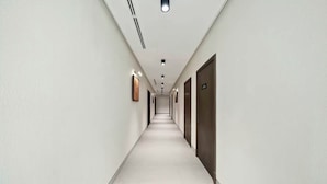 A long, narrow hallway with doors on both sides, recessed lighting, and a white floor. - emaro hostel (Dubai)