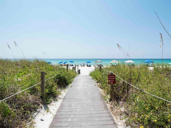 A wooden pathway leading to a beach with umbrellas and lounge chairs.