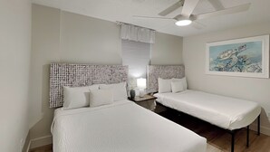 Ein Zimmer mit zwei Betten, einem Deckenventilator, einem Gemälde und einem Fenster mit Jalousien.