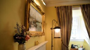 A room with a fireplace, a framed picture, a vase with flowers, and a lamp. - Barcaldine Castle (Oban)