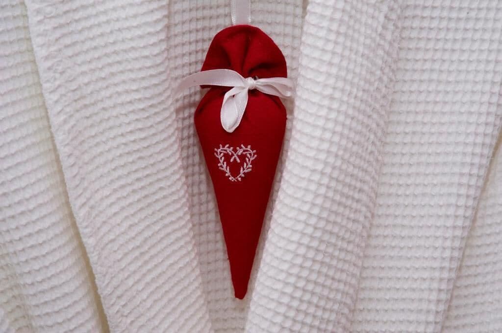 A red object with a white ribbon and a heart design, hanging on a textured white surface.