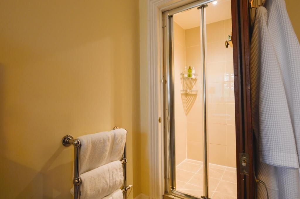 A bathroom with a glass shower door, a towel rack with two towels, and a glass shelf with toiletries.
