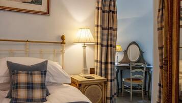 A bedroom with a bed, a bedside table with a lamp, a chair, a desk with a mirror, and curtains.