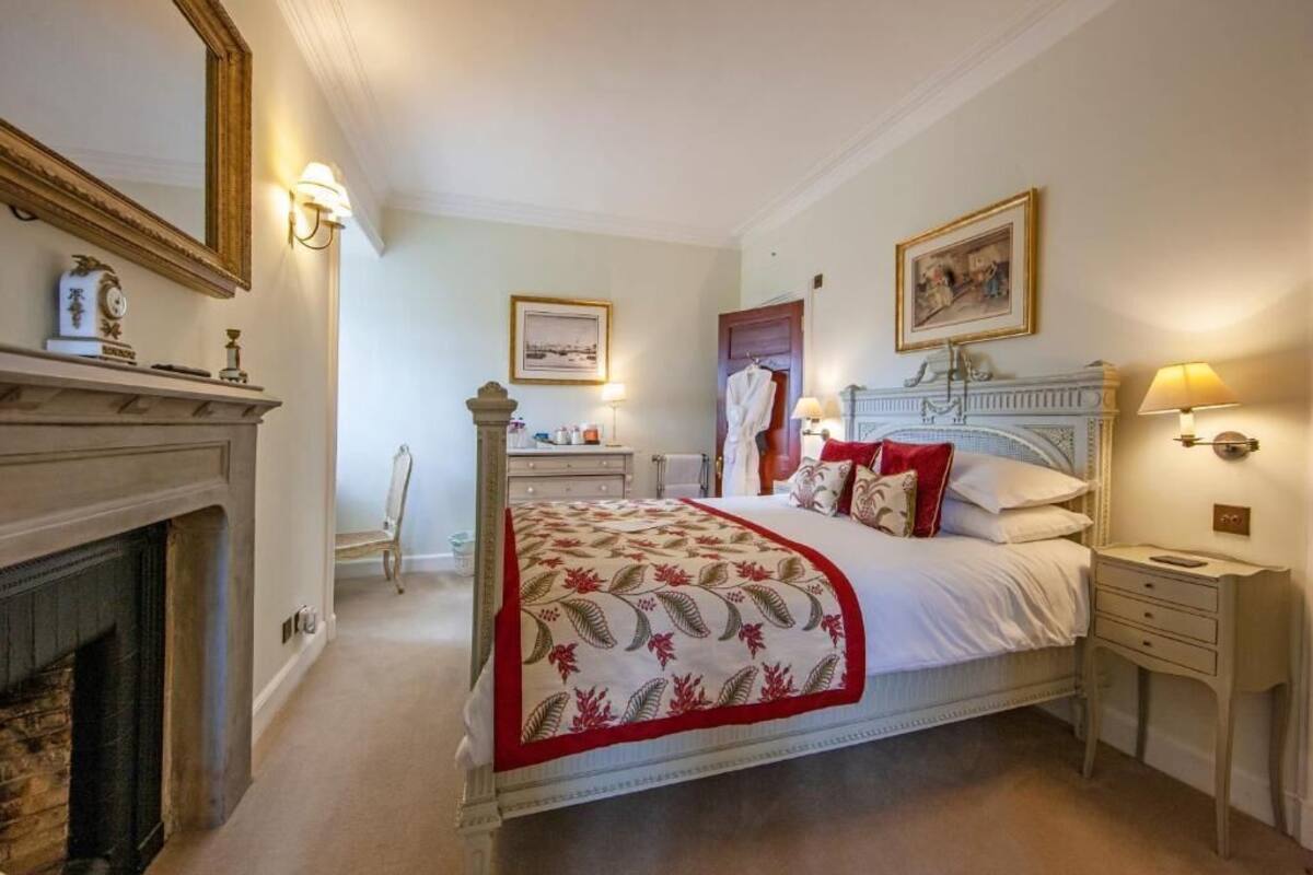 A bedroom with a bed, bedside tables, a fireplace, and wall-mounted lighting.