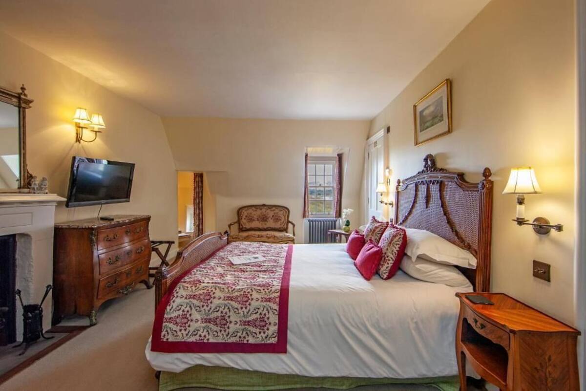 A bedroom with a large bed, a television, a dresser, and a fireplace.