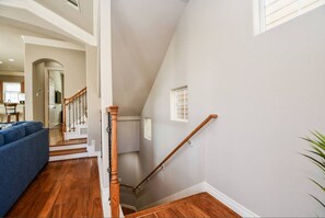 A staircase with a wooden handrail, a blue sofa, and a kitchen in the background. - Fully Furnished 3BR / 3BA Home Near Medical Center (Houston)