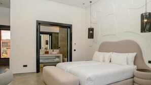 Un dormitorio moderno con una cama grande, un banco, un tocador con espejo y una lámpara colgante.