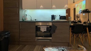 Eine moderne Küche mit eingebautem Ofen, ein Essbereich mit Tisch und Stühlen sowie ein Projektorbildschirm, der eine Naturansicht zeigt.