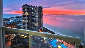 Een hoog hotel met een zwembad, met uitzicht op een wateroppervlak en een zonsondergang.