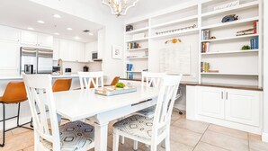 Een moderne keuken met witte kasten, een centraal eiland en een eetgedeelte met witte stoelen.
