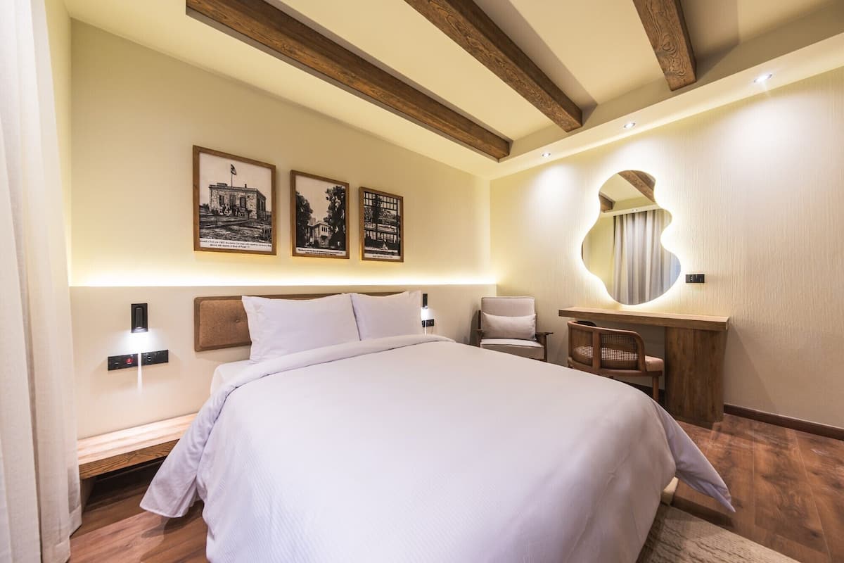 A hotel room with a large bed, a desk with a mirror, and wall-mounted artwork.