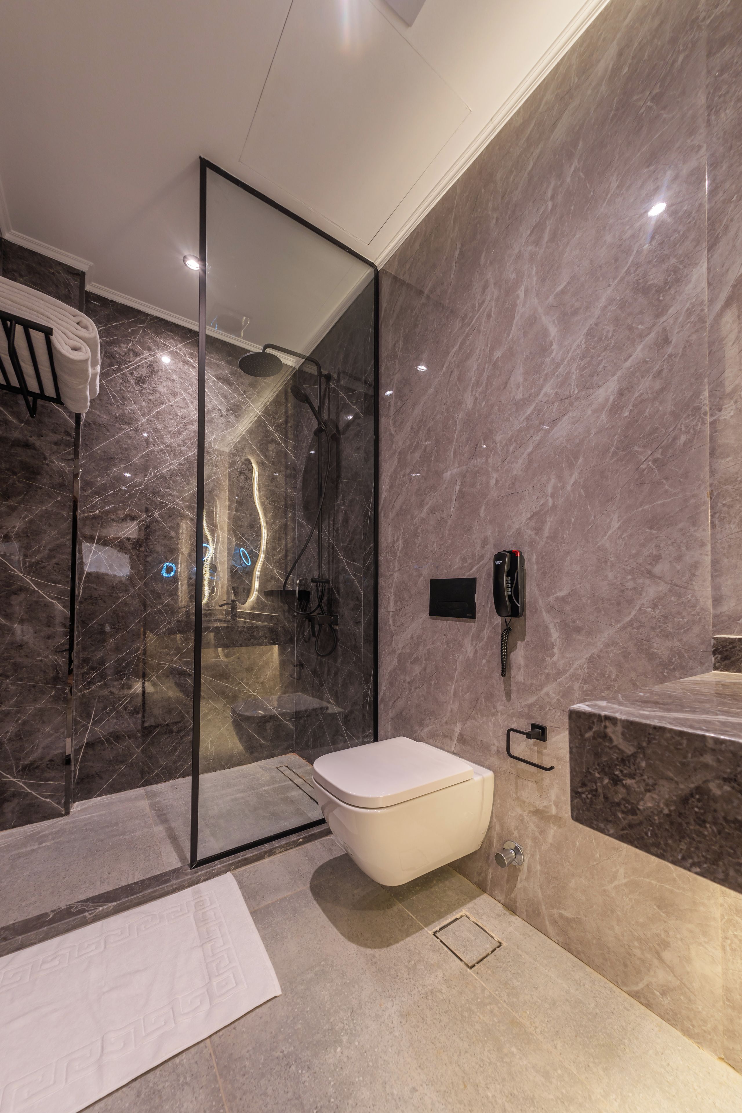 A modern bathroom with a glass-enclosed shower, a white toilet, and a marble wall.