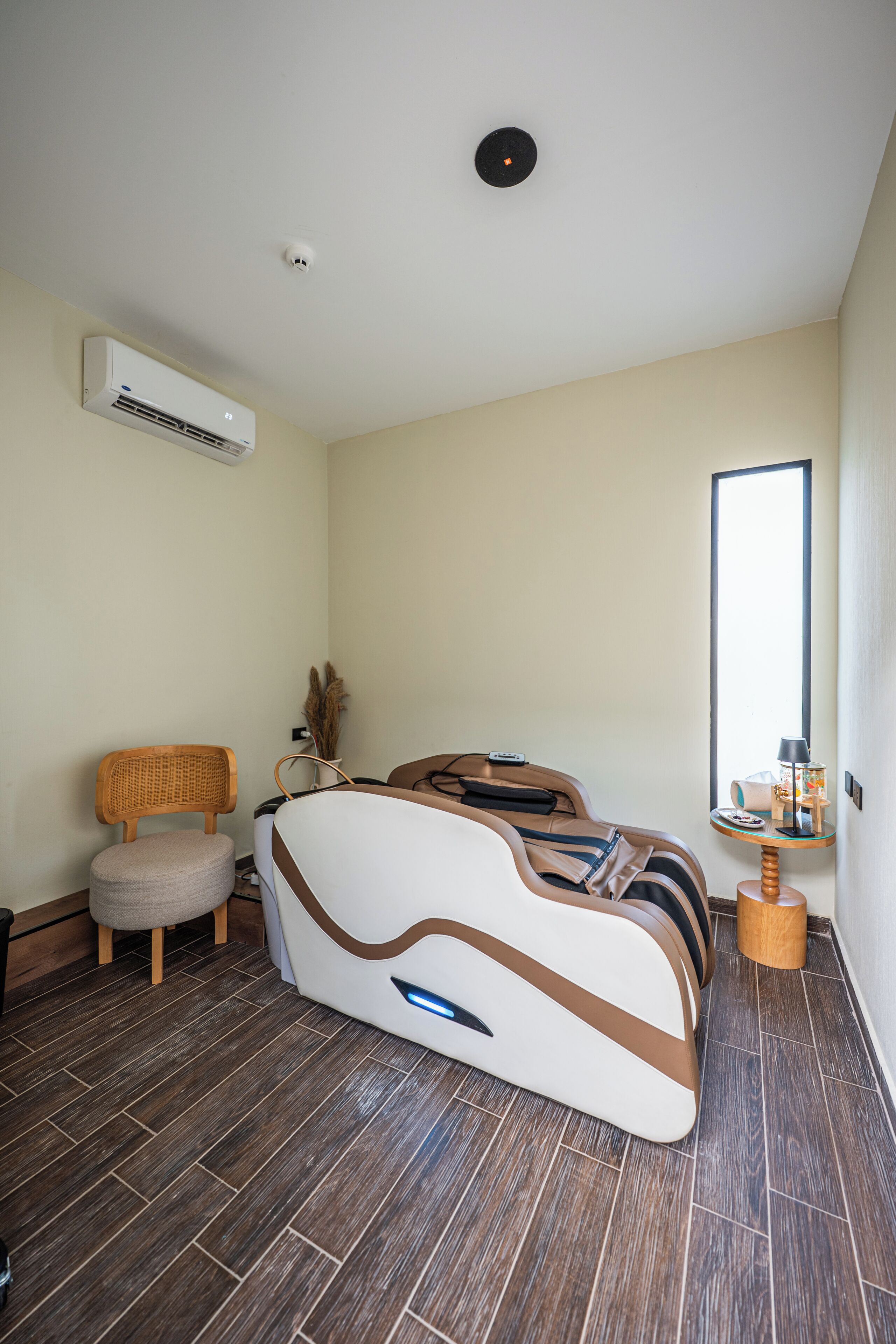 Moderni hotellihuone, jossa on ainutlaatuinen sängyn muotoilu, tuoli, pieni pöytä lampun kanssa ja ilmastointilaite.