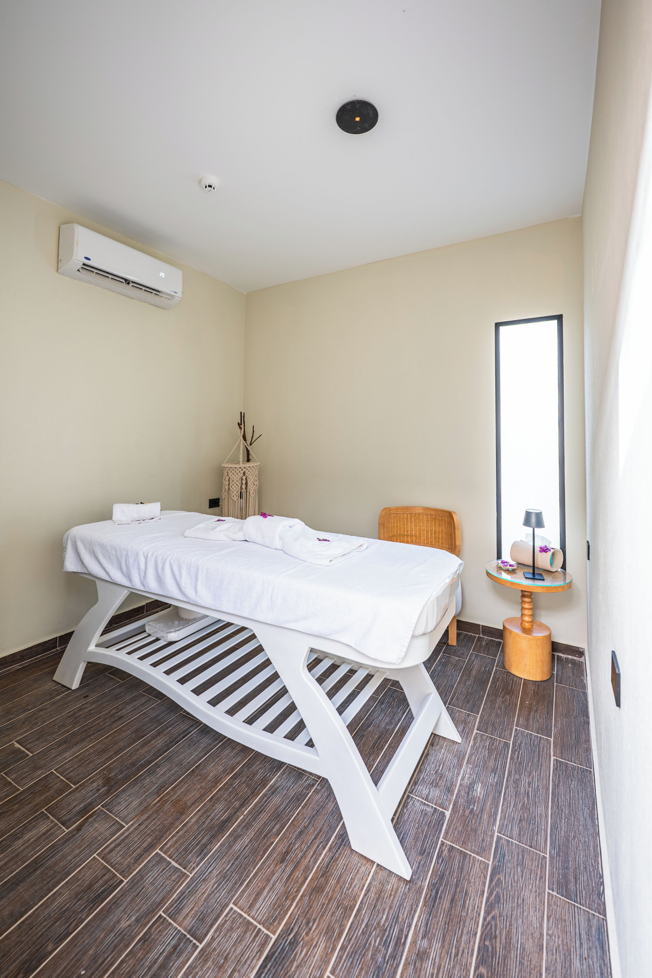 Una habitación con una cama, una mesita, una silla, un espejo y un equipo de aire acondicionado.