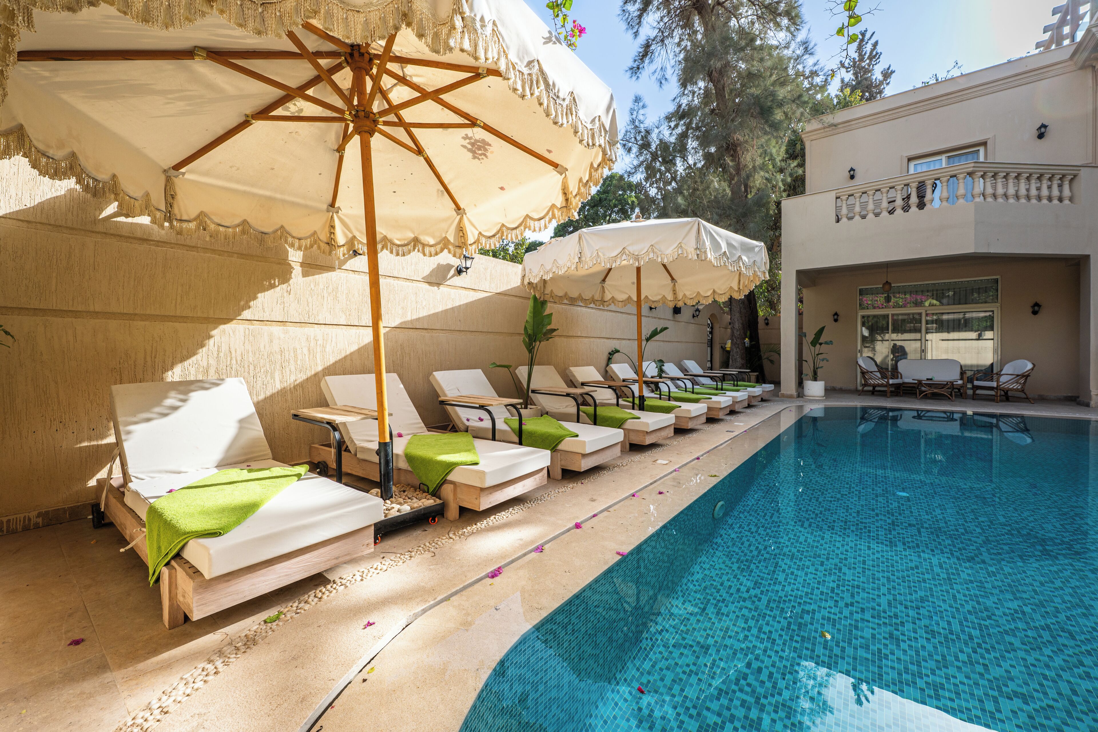 A poolside area with lounge chairs and umbrellas, a clear pool, and a building with a balcony.