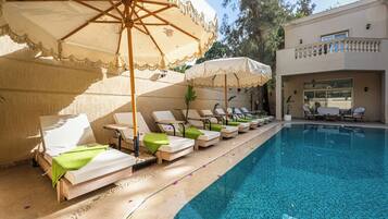 Un espace aménagé au bord de la piscine, avec des chaises longues et des parasols, une piscine à eau claire et un bâtiment doté d’un balcon.