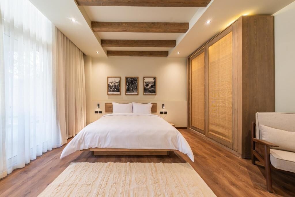 A bedroom with a large bed, wooden beams, a sofa, and a large window with curtains.