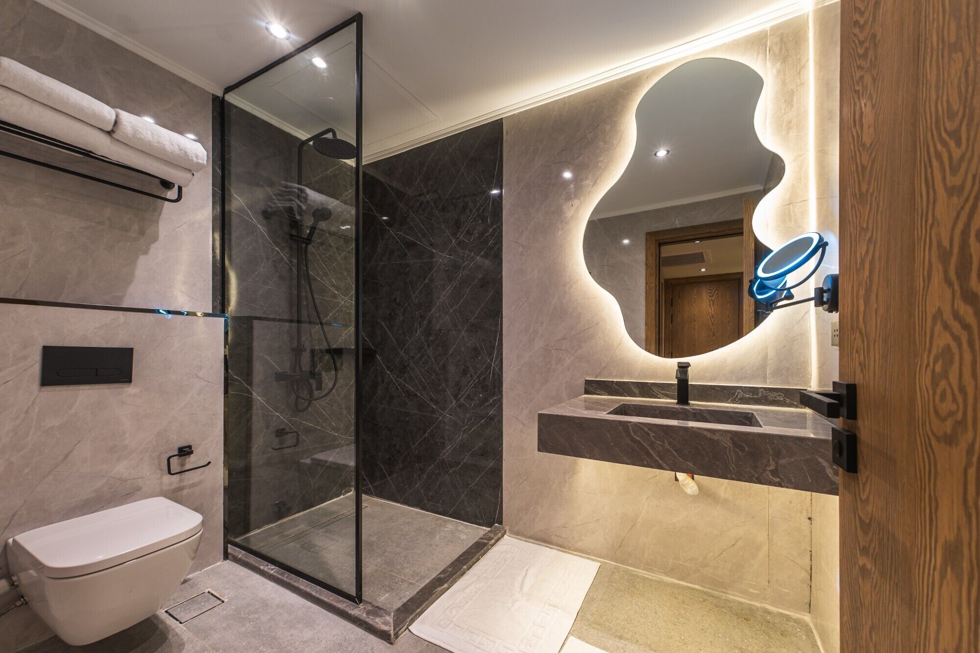 A modern bathroom with a glass-enclosed shower, a toilet, a sink with a marble countertop, and a large mirror with a wooden frame.