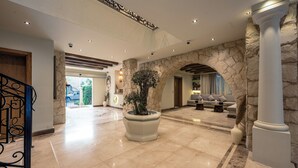 Eine großzügige Lobby mit einem steinernen Bogen, einem großen Kübelbaum und einer Sitzecke mit Sofas.