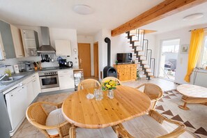 Una cucina moderna con piano cottura, lavello e pensili, una zona pranzo con tavolo in legno e sedie in vimini, e una scala che conduce a un piano superiore.