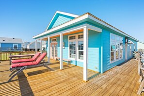 Una casa de playa con terraza de madera, porche cubierto y zona de piscina.