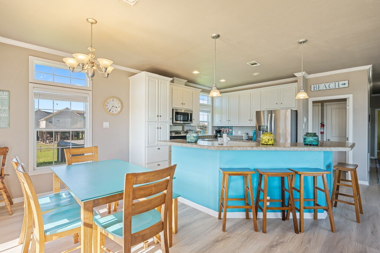Une cuisine moderne avec des meubles blancs, un îlot central bleu, des chaises en bois et des luminaires suspendus.