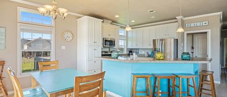 Une cuisine moderne avec des meubles blancs, un îlot central bleu, des chaises en bois et des luminaires suspendus.