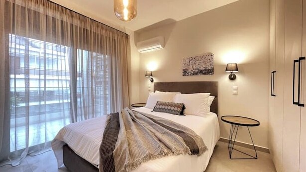 A bedroom with a bed, curtains, a wall-mounted lamp, and a small table. - Athenean Gem Near Athens Metro Mall-B2 (Ilioupoli)