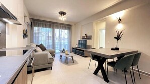 A modern living room with a sofa, coffee table, dining table with chairs, and a TV. - Athenean Gem Near Athens Metro Mall-B2 (Ilioupoli)