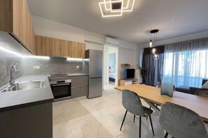 Eine moderne Küche mit Edelstahlgeräten, ein Essbereich mit Holztisch und Stühlen sowie ein Wohnbereich mit Fernseher und Vorhängen.