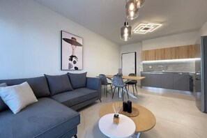 Ein modernes Wohnzimmer mit grauem Sofa, einem runden Couchtisch und einem Essbereich mit Stühlen.