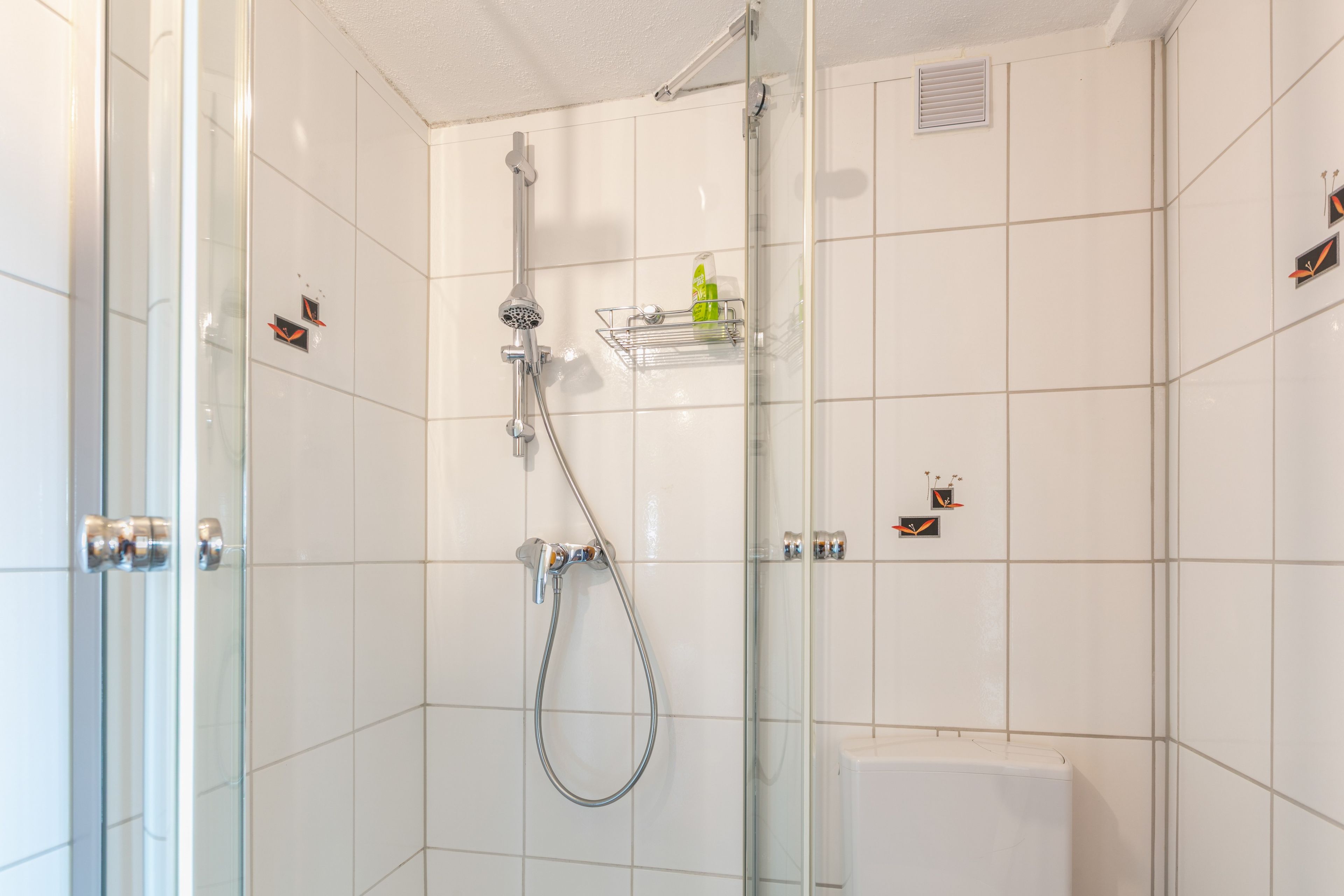 Un baño moderno con cabina de ducha de vidrio, cabezal de ducha manual y grifo empotrado en la pared.