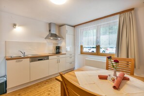A compact kitchen with a dishwasher, a coffee maker, and a window with curtains. - Alpenblick Apartment (Todtnau)