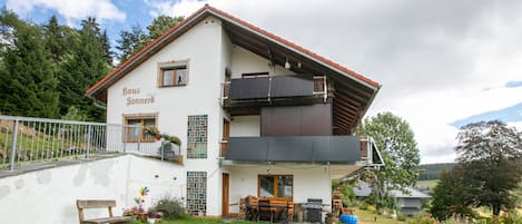 A two-story house with a balcony, a wooden bench, and a garden.