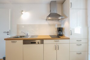 A compact kitchen with a built-in dishwasher, a coffee maker, and a stainless steel range hood. - Alpenblick Apartment (Todtnau)