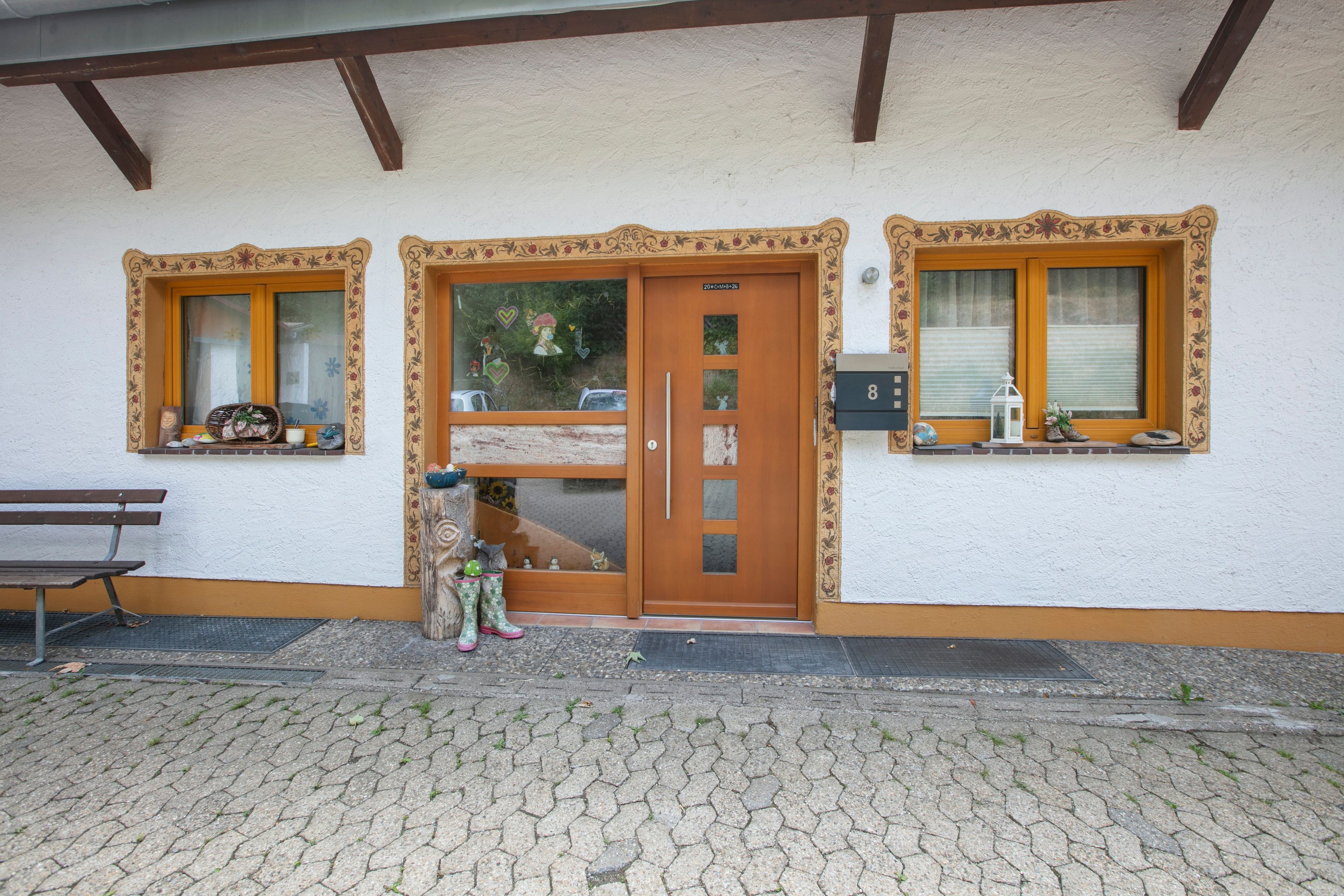 A building with a wooden door, two windows with shutters, a bench, and a small garden area.