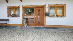 A building with a wooden door, two windows with shutters, a bench, and a small garden area. - Alpenblick Apartment (Todtnau)