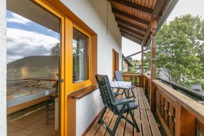 A balcony with a wooden floor, a table with chairs, and a bed with a floral bedspread. - Alpenblick Apartment (Todtnau)