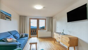 A modern living room with a sofa, a wooden desk, and a view through a glass door. - Alpenblick Apartment (Todtnau)