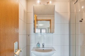 Un bagno con un lavandino bianco, uno specchio sopra e una zona doccia sulla destra.