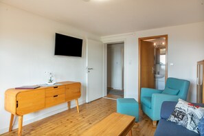 A modern living room with a wooden cabinet, a teal armchair, a small table, and a flat-screen TV mounted on the wall. - Alpenblick Apartment (Todtnau)