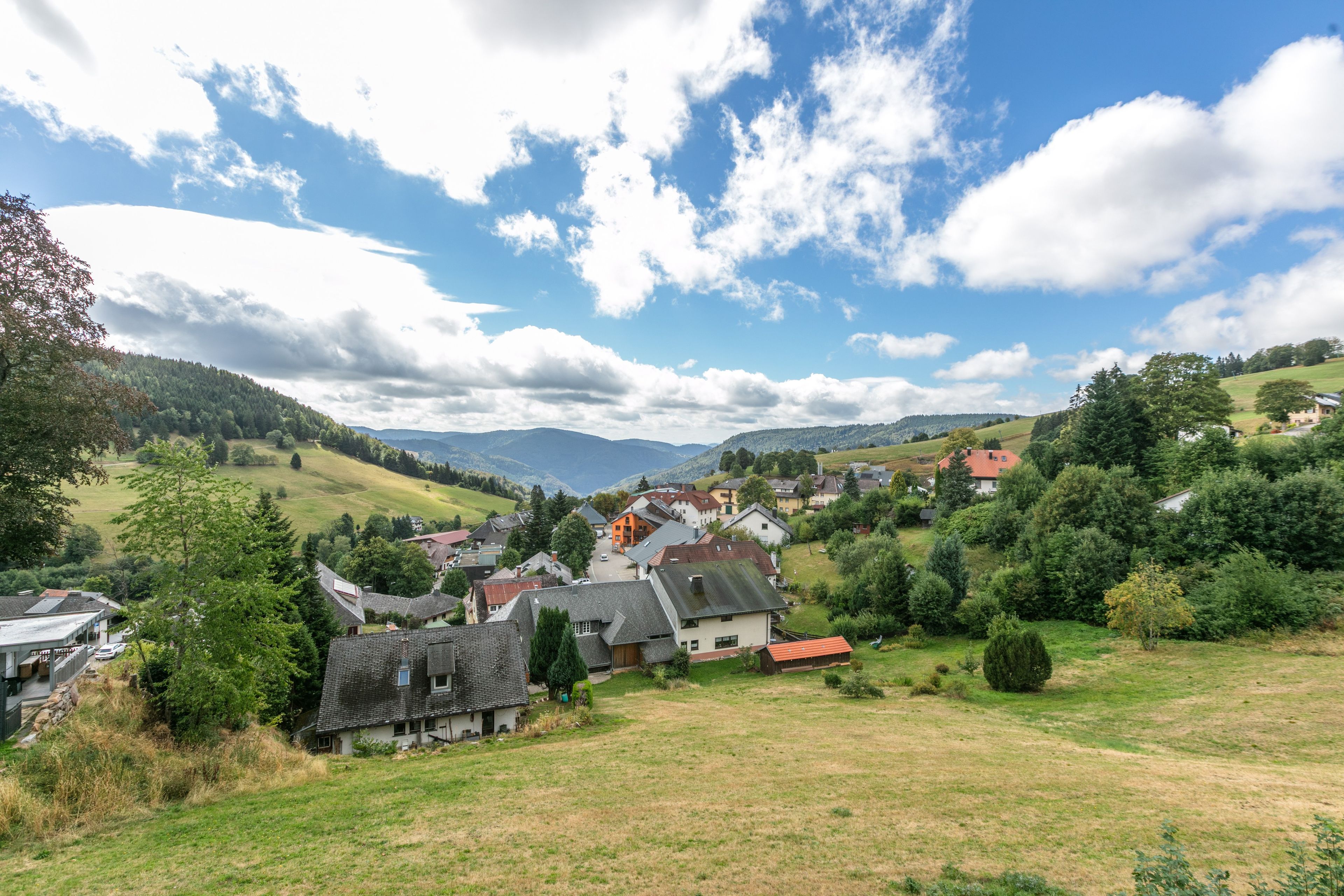 A village with traditional houses, a clear sky, and surrounding hills.
