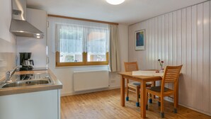 A compact kitchen with a built-in stove, a sink, and a window with sheer curtains. - Alpenblick Apartment (Todtnau)