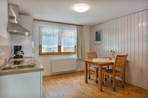 Cocina compacta con estufa integrada, lavamanos y ventana con cortinas de gasa.