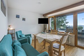 A modern living room with a teal sofa, a wooden dining table, and a large window offering a view of trees and hills. - Wiesentalblick Apartment with Mountain View and Balcony (Todtnau)