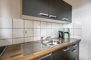 A modern kitchen with a stainless steel sink, a wooden countertop, and a green coffee maker.