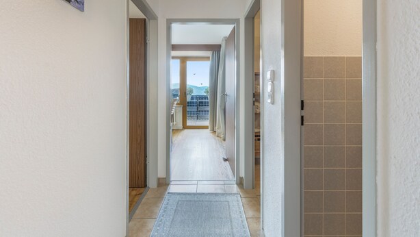 En hall som leder ut till en balkong med utsikt över himlen och avlägsna byggnader.