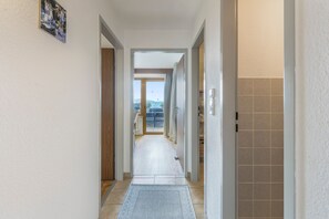A hallway leading to a balcony with a view of the sky and distant buildings.