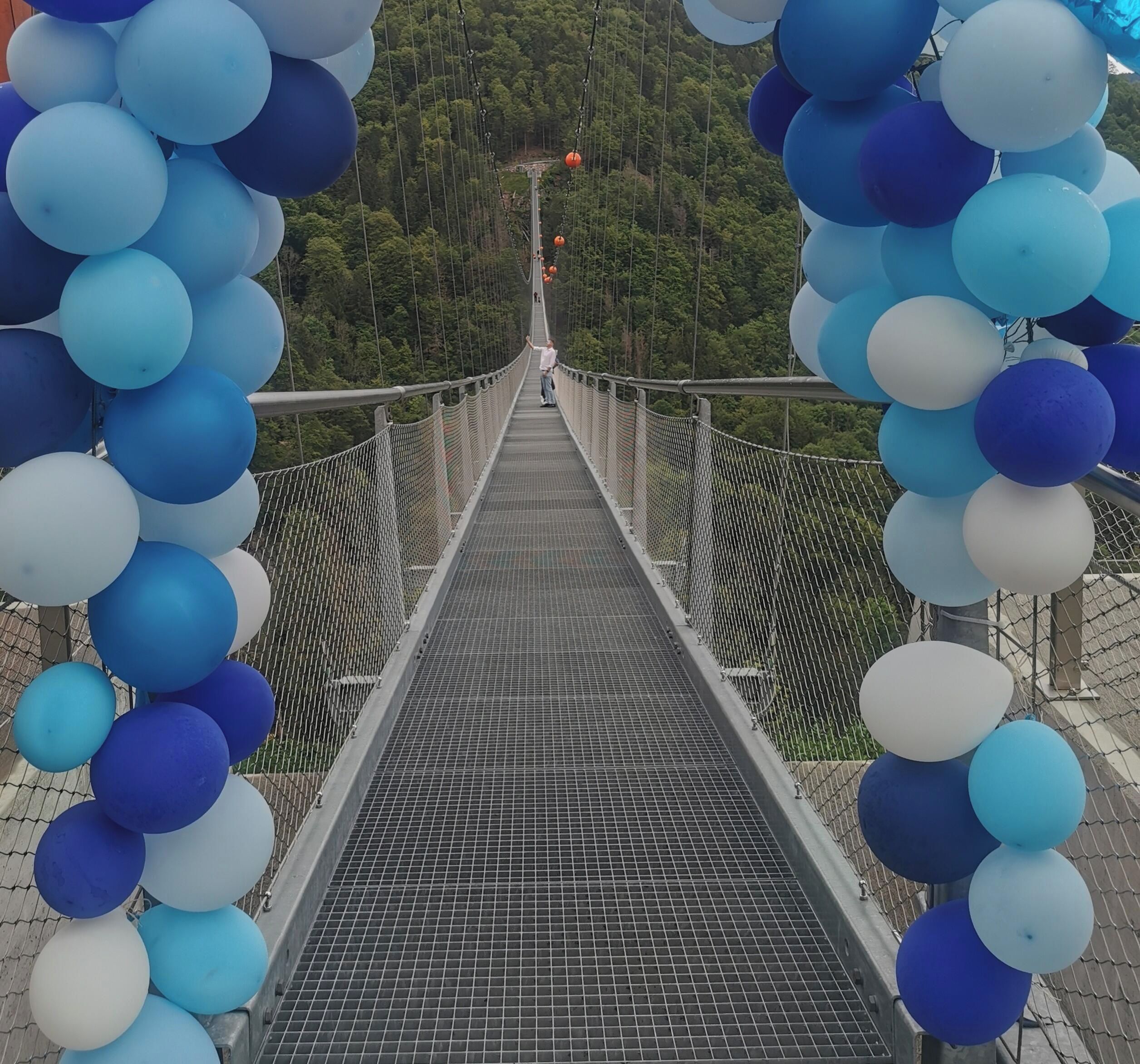 Un puente colgante con pasarela de malla, rodeado de globos.